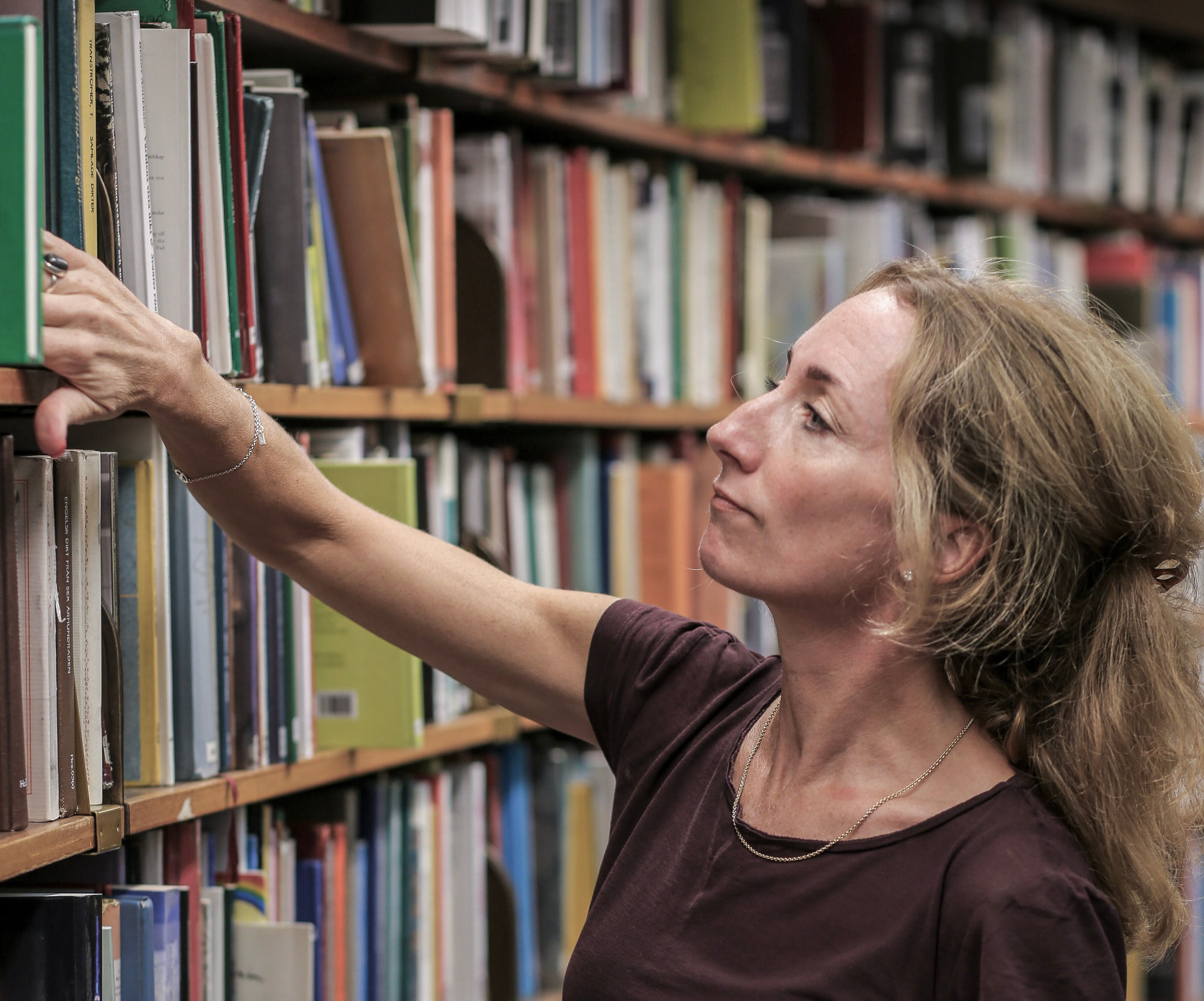 Pia reaching for a book from a shelf, her face lifted toward it