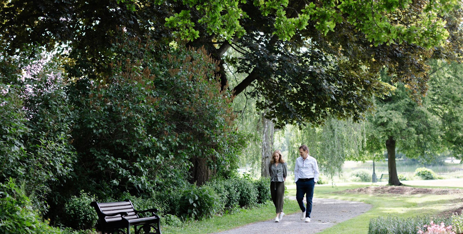 Pia walking with a companion along a gravel path through a leafy park